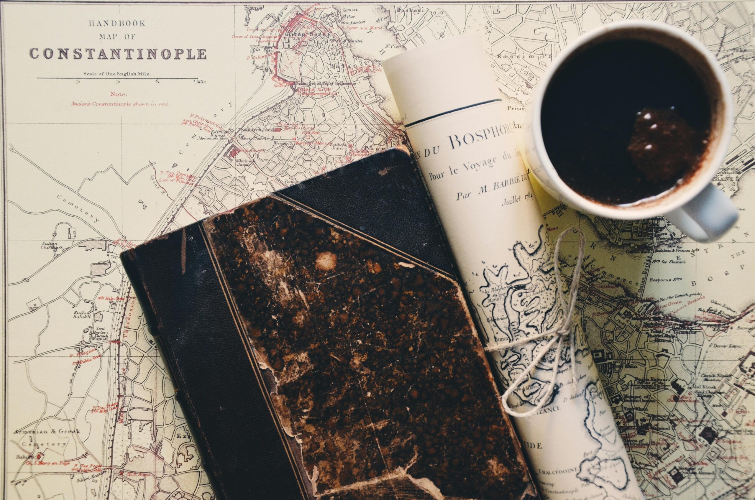 Vintage map of Constantinople with an old book, a rolled-up map, and a cup of coffee placed on top