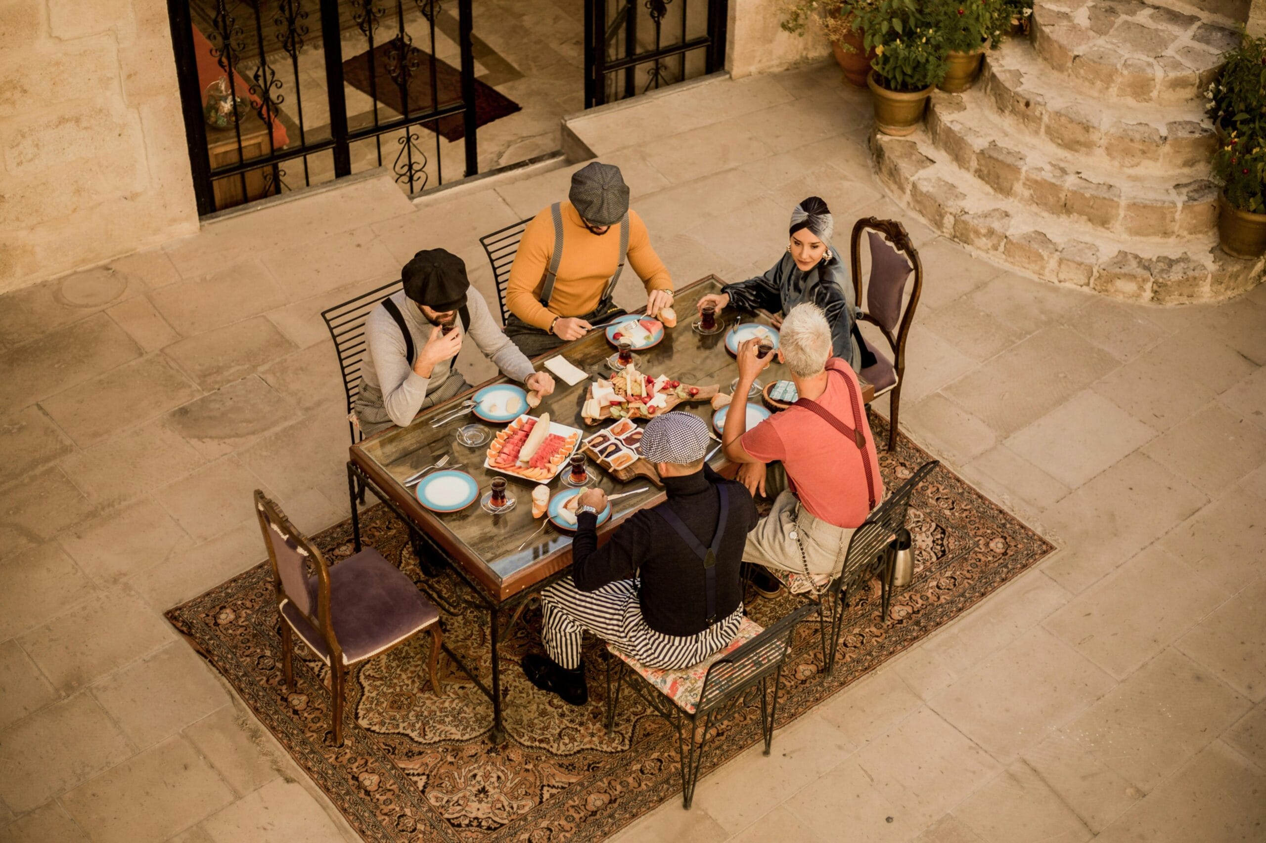 Group of friends enjoying a traditional Turkish breakfast outdoors, seated around a table adorned with vibrant dishes and tea glasses in a rustic courtyard setting.