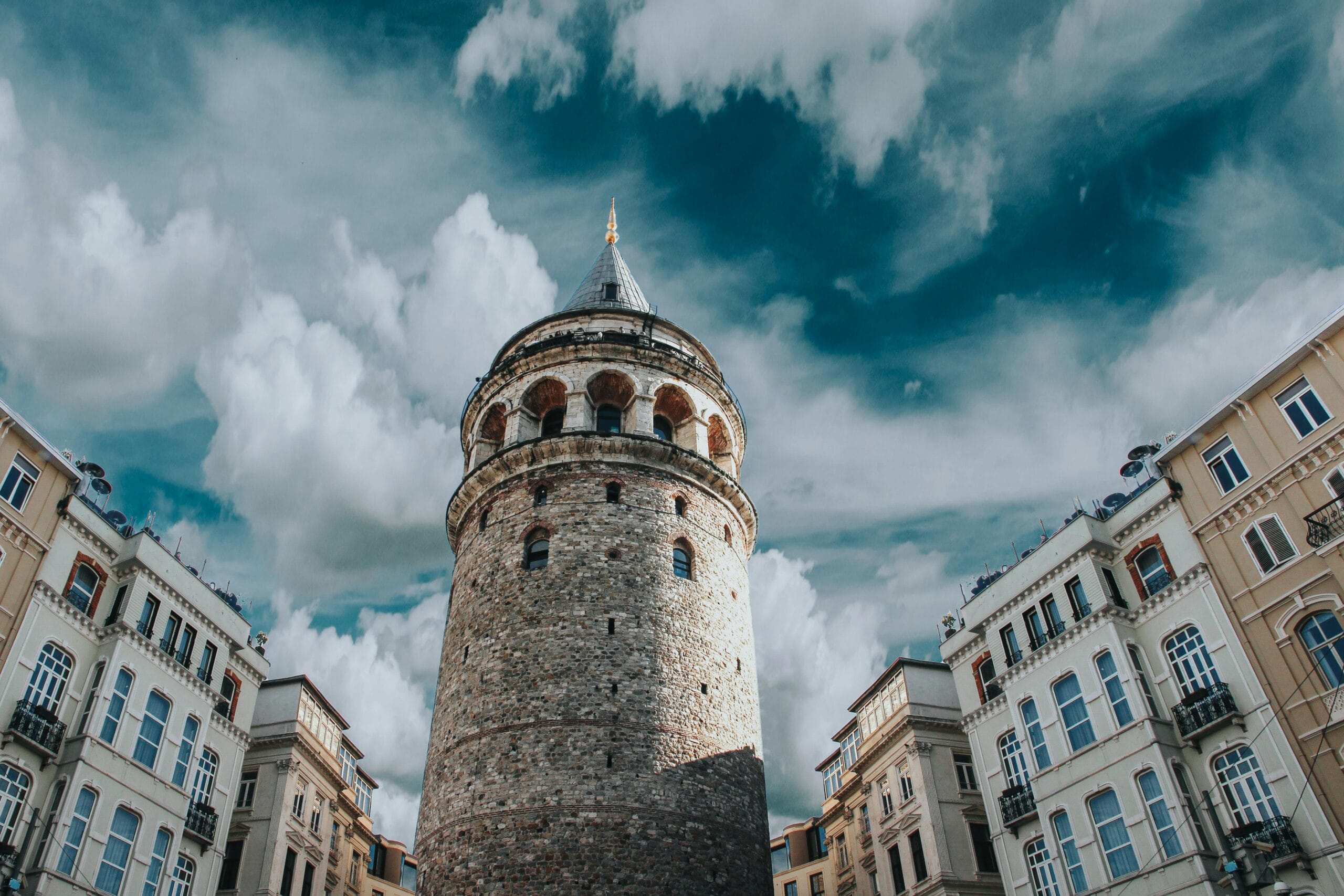 Galata Tower surrounded by charming historic buildings under a dramatic, cloudy sky in Istanbul, Turkey. perfect for turkey group travel