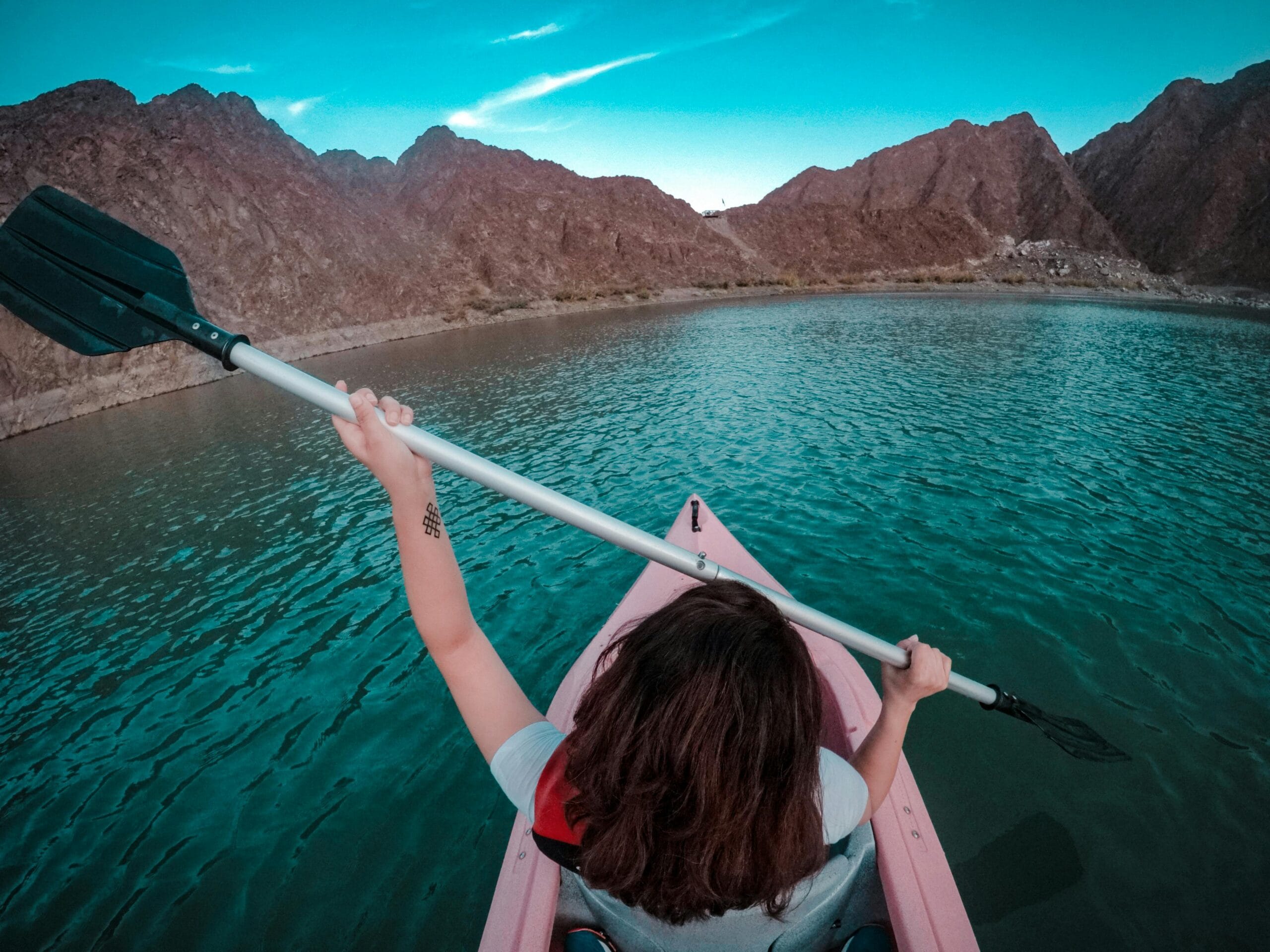A person kayaking on the calm turquoise waters of Hatta Dam, surrounded by rugged mountains under a vibrant sky. Best Dubai DMC