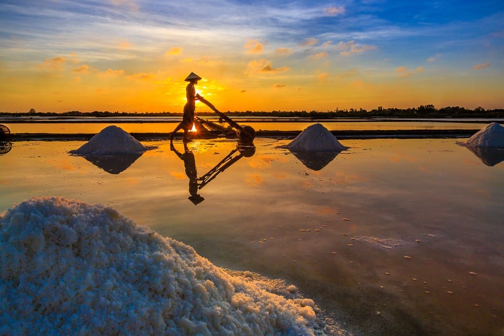 Salt workers harvesting at Quảng Bình salt fields in Vietnam, an authentic cultural journey designed by the best DMC for Vietnam.