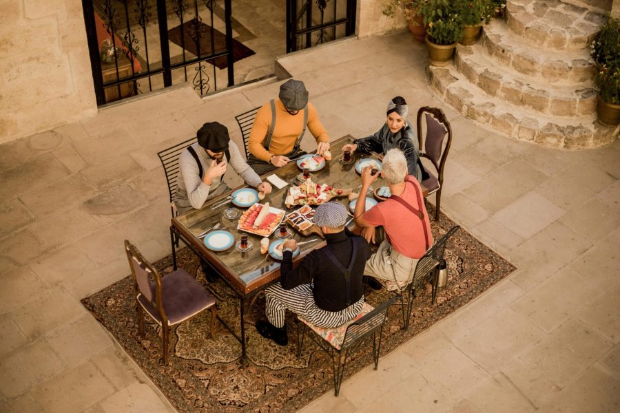 Group of friends enjoying a traditional Turkish breakfast outdoors, seated around a table adorned with vibrant dishes and tea glasses in a rustic courtyard setting.